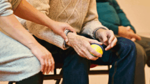 Holding an elderly man's hand while he holds an exercise ball