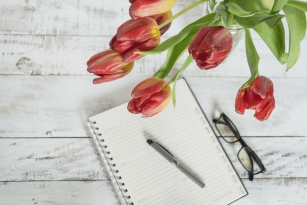 Table with flowers, reading glasses, notepad, and pen