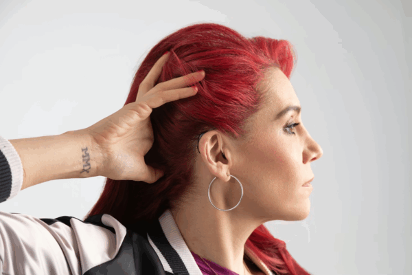 Young woman with red hair and tatoos displaying her hearing aid