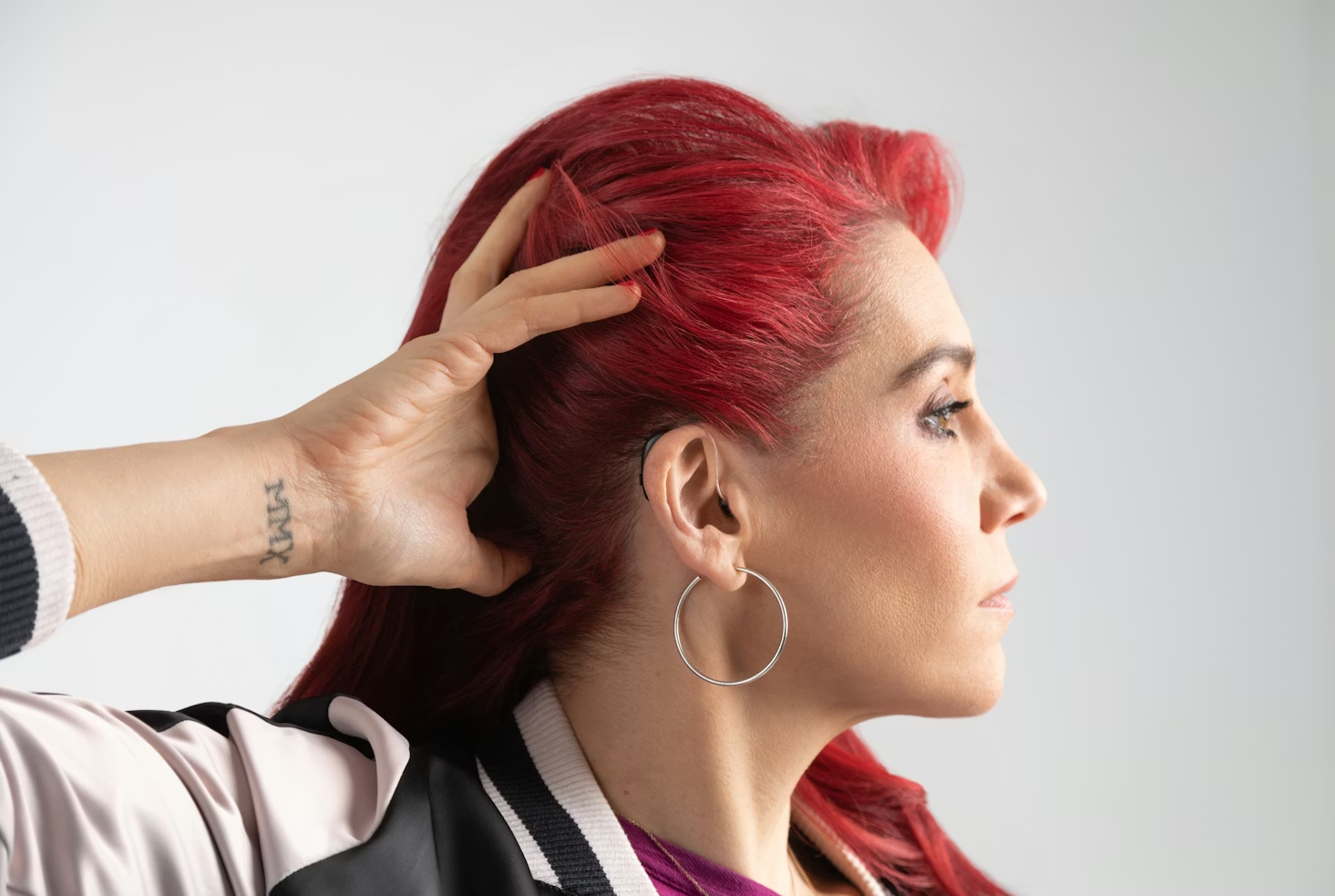 Young woman with red hair and tatoos displaying her hearing aid